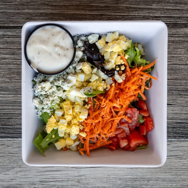 Fresh salad with lettuce, blue cheese, chopped eggs, shredded carrots, diced tomatoes, and creamy dressing.