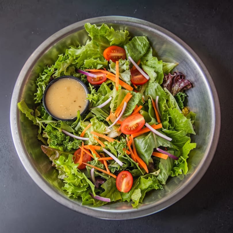 Fresh garden salad in a metal bowl with mixed greens, cherry tomatoes, carrots, and dressing.