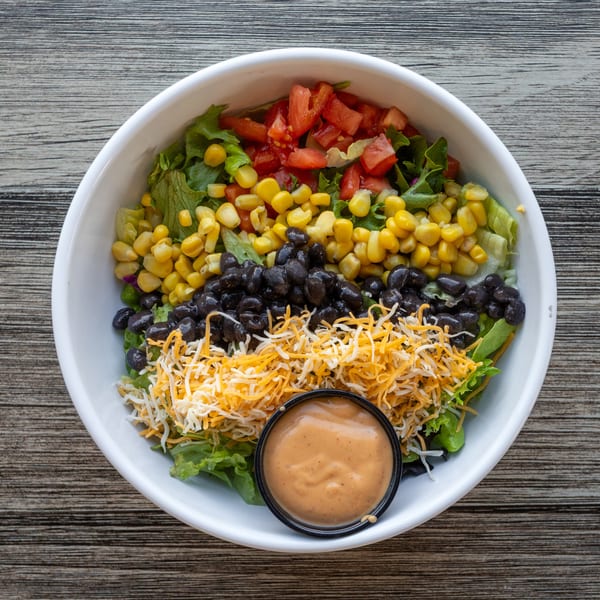 Overhead view of a salad with lettuce, tomatoes, corn, black beans, shredded cheese, and dressing.