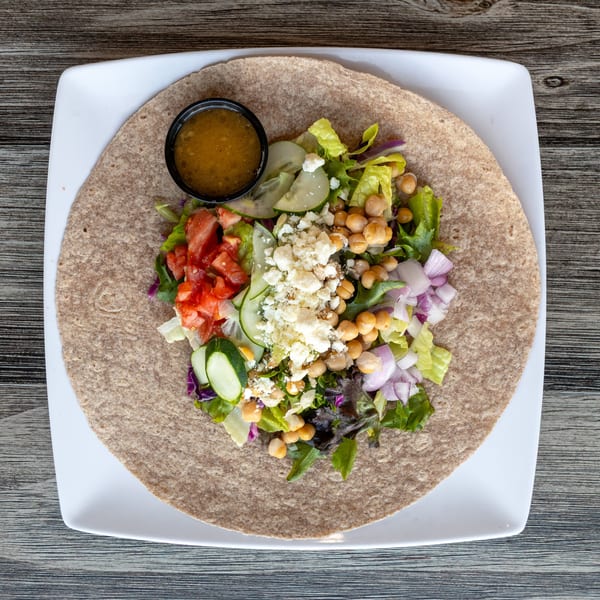 Colorful salad wrap with chickpeas, feta, tomatoes, cucumbers, and dressing on a white plate.