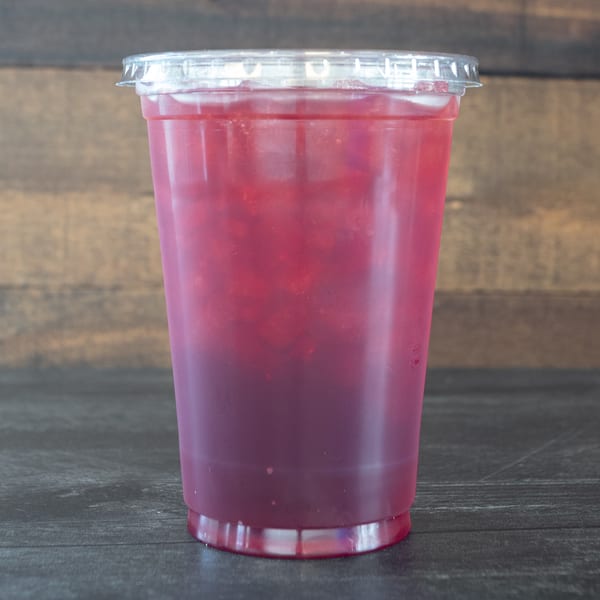 A vibrant red iced drink in a clear plastic cup with a lid, against a wooden background.