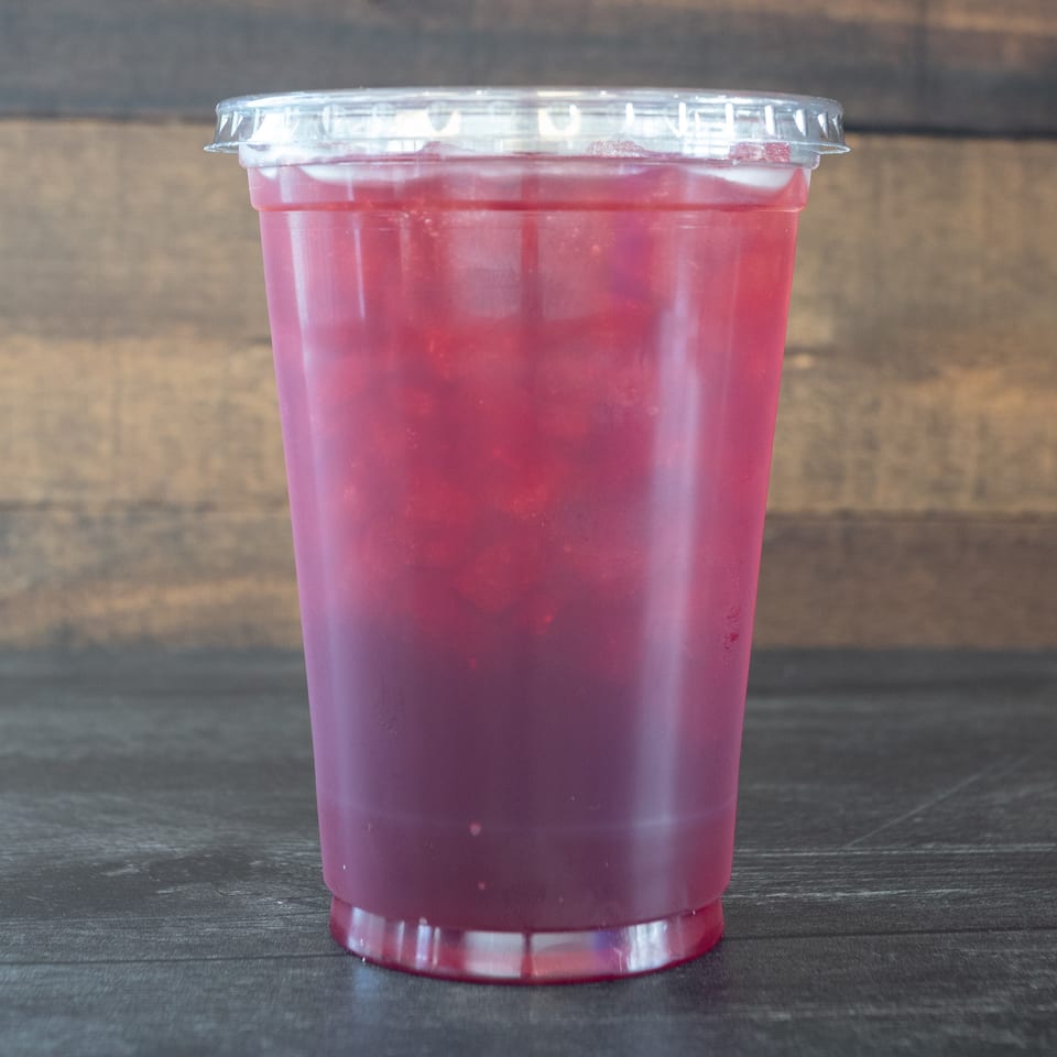 A vibrant red iced drink in a clear plastic cup with a lid, against a wooden background.