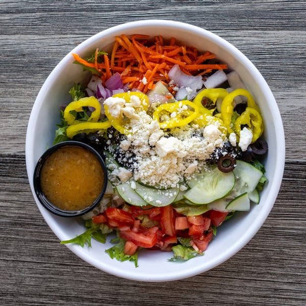 Colorful salad with lettuce, carrots, peppers, olives, feta, and dressing in a white bowl.